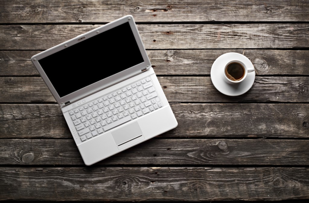 White laptop with coffee cup on old wooden table.