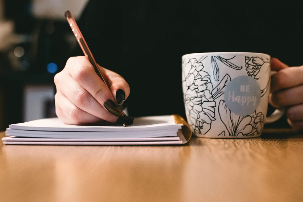 Person writing in a notebook with a mug in hand