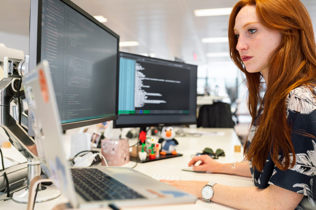 Web developer coding at her desk with multiple screens