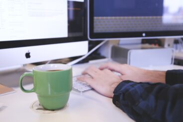 Typing on keyboard with two IMAC screens and a cup of coffee